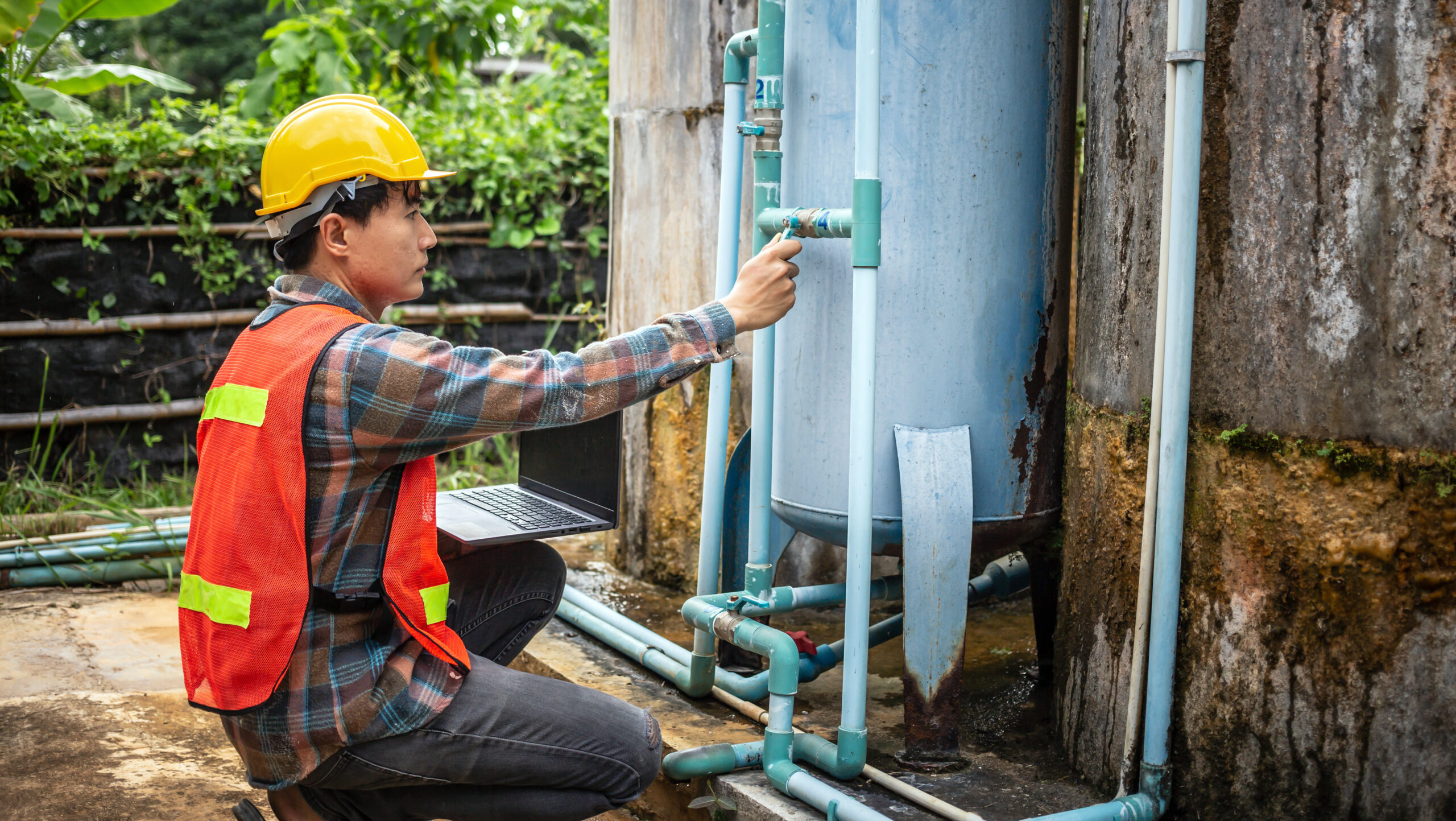 Engineer working in drinking water factory using a laptop computer to check water management system and boiler water pipe  outside the factory