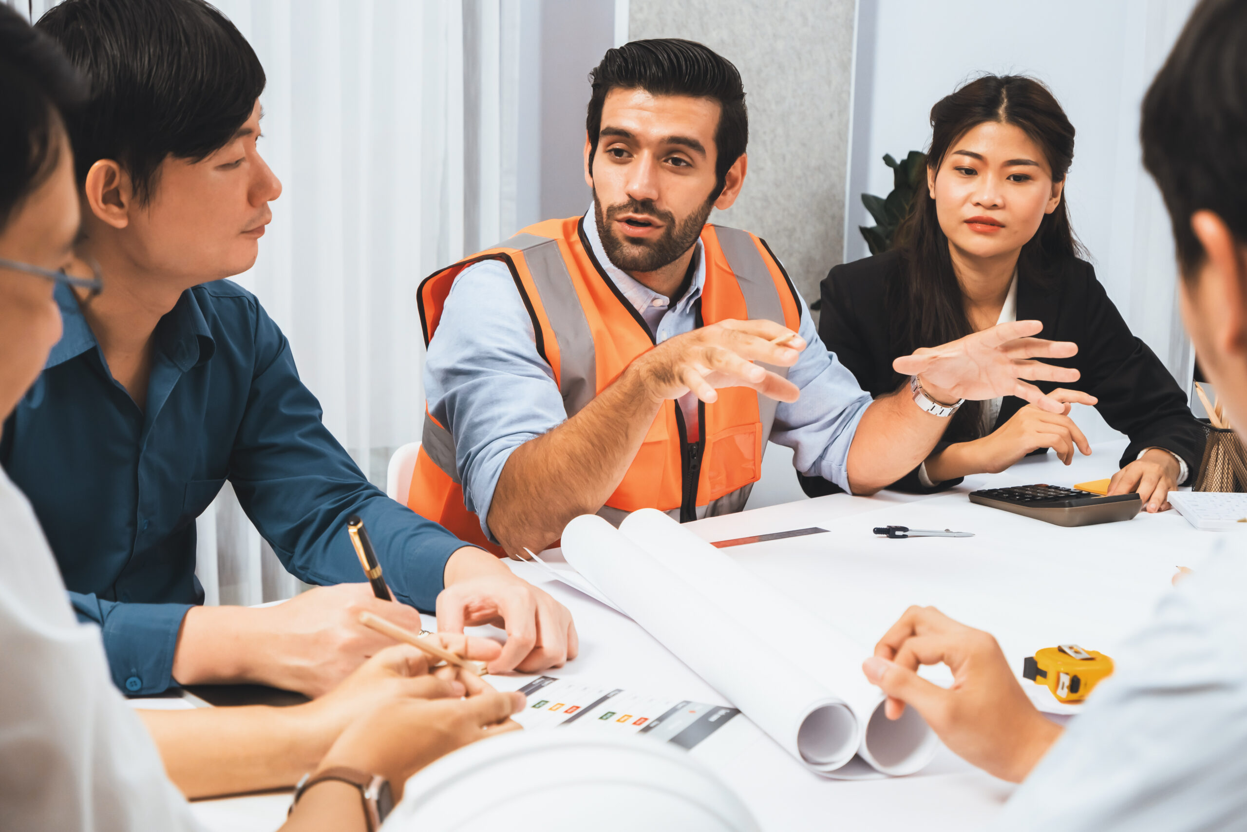 Diverse group of civil engineer and client working together on architectural project, reviewing construction plan and building blueprint at meeting table. Prudent