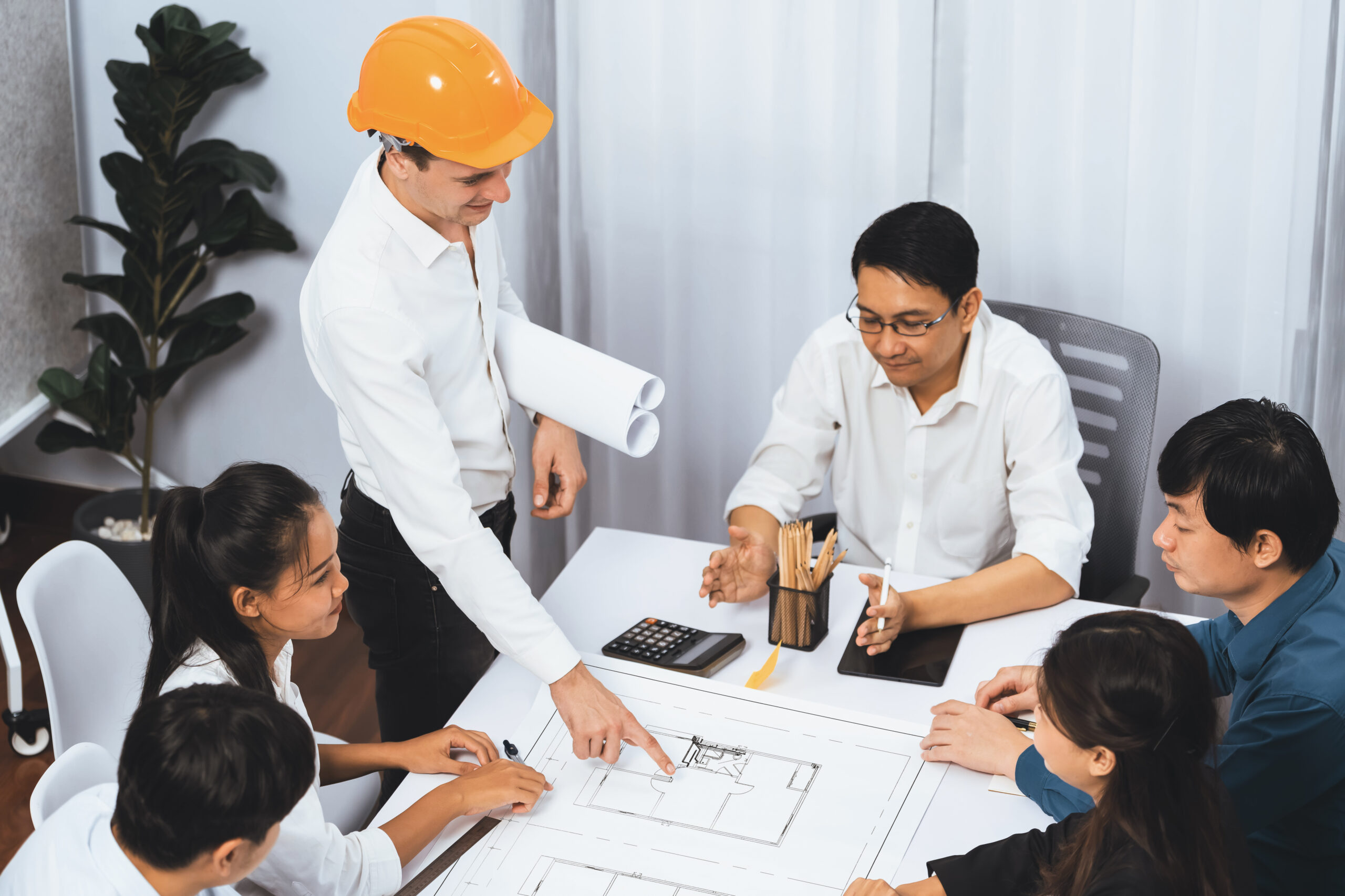 Diverse group of civil engineer and client working together on architectural project, reviewing construction plan and building blueprint at meeting table. Prudent