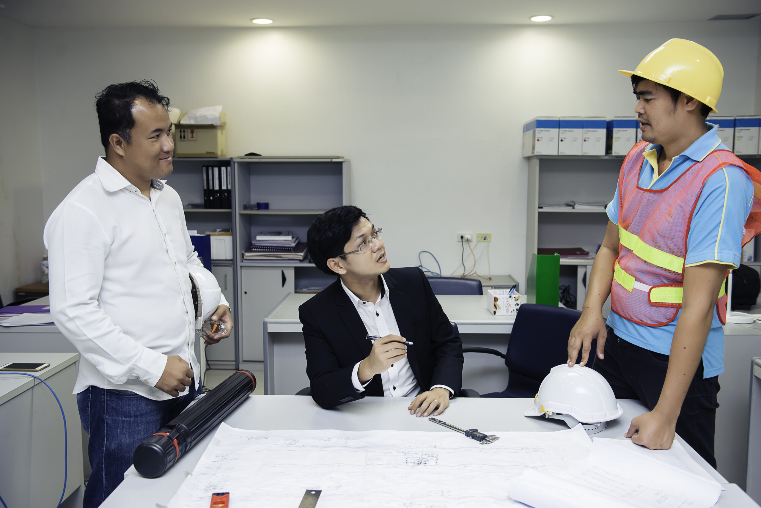 Three asian engineers looking paper plan of the building,Discuss about the problems and solutions of the construction in the office,Customer complaints engineers about green building send no on schedule